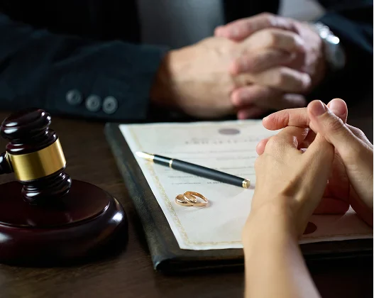 Gavel, wedding rings, and legal document on a table with a lawyer and client discussing divorce or legal separation